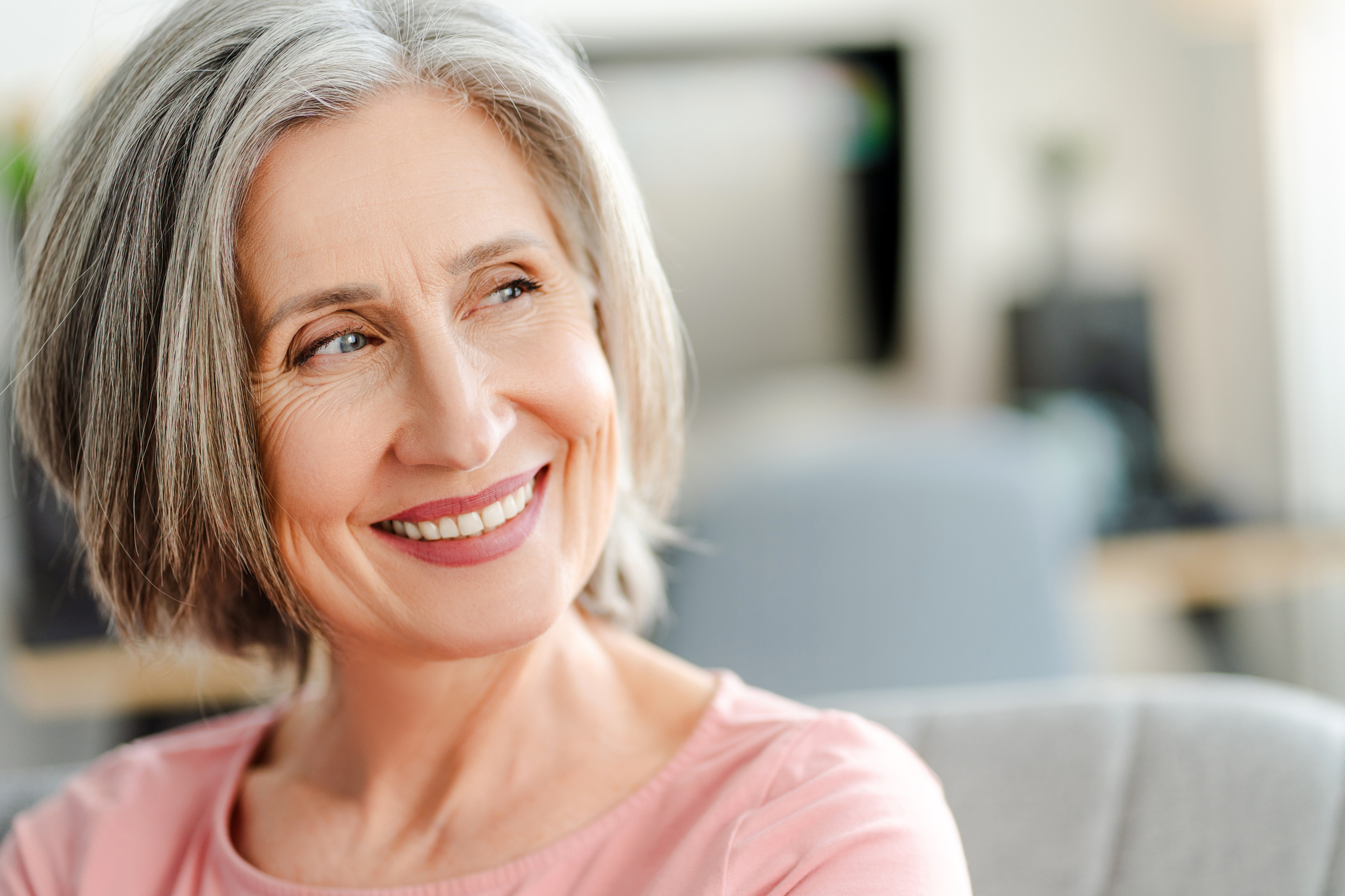 Smiling confident senior woman sitting on comfortable sofa at home. Happy female looking away